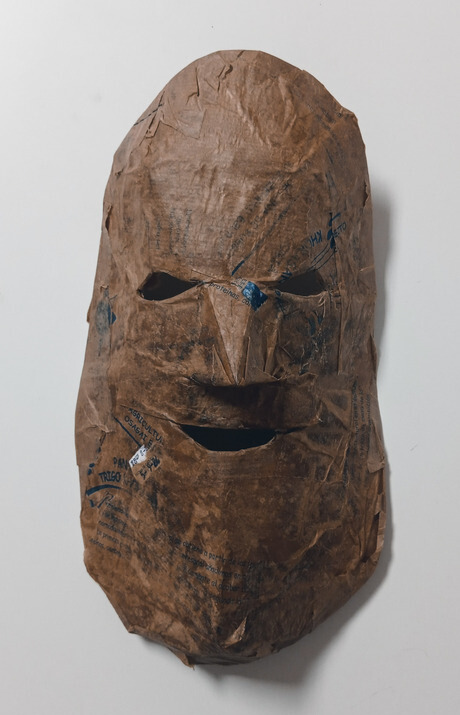 Mascara-de-carton-encolado-marron-sobre-pared-blanca Mascara-de-carton-encolado-marron-sobre-pared-blanca